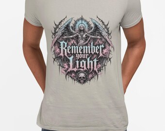 May include: A light gray short-sleeve t-shirt featuring a graphic print of a winged figure with arms outstretched above a skull. The design includes intricate gothic-style linework in shades of blue and pink, with the text "Remember your Light" centered.