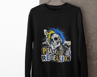 May include: A black long-sleeve sweatshirt featuring a graphic print of a skull with blue and yellow spiky hair. The skull has decorative markings and a peace sign symbol. Below the skull, the text reads PEACE IS REBELLION in bold letters.