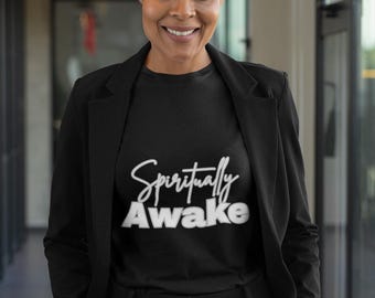 May include: A black t-shirt with the words "Spiritually Awake" in white script. The person is wearing a black blazer and black pants. The image is taken indoors with a blurred background.
