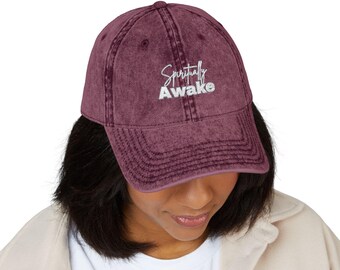 May include: A burgundy baseball cap with the embroidered text "Spiritually Awake" in white. The cap has a curved brim and a vintage, worn look. The hat is made of a soft, textured material.