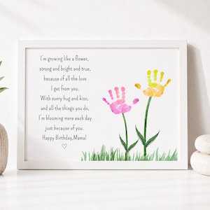May include: A framed print with a white border displays a poem and handprint art. The poem begins, "I'm growing like a flower...Happy Birthday, Mama!" Two handprints, one pink and one yellow, are shown as flowers with green stems.