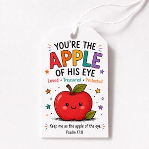 May include: A white rectangular gift tag with a string, featuring a red apple illustration with a smiling face. The text reads: YOU'RE THE APPLE OF HIS EYE, Loved, Treasured, Protected, and Keep me as the apple of the eye. Psalm 17:8, with colorful stars.