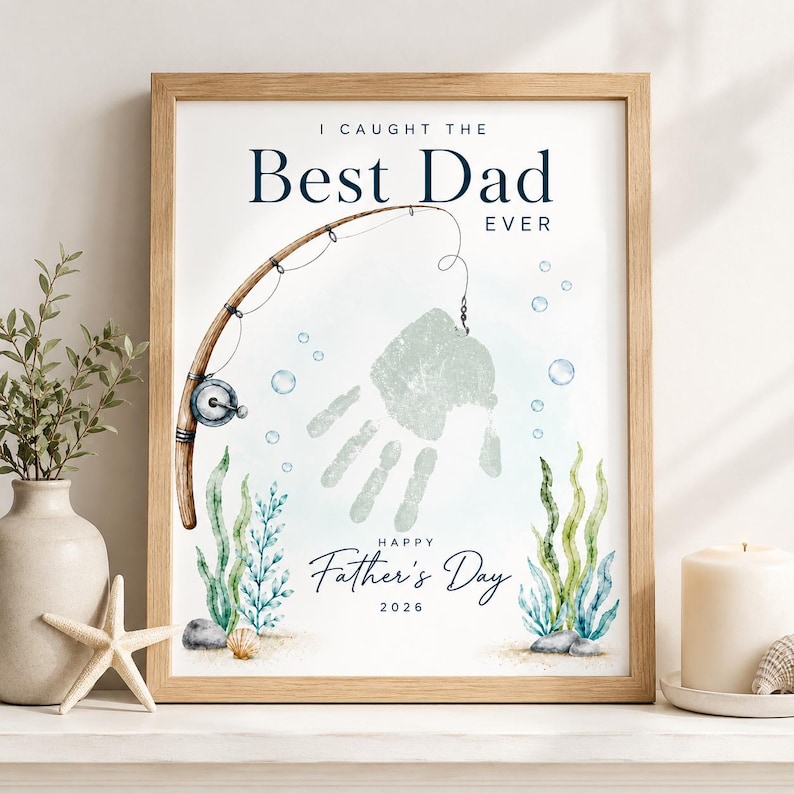 May include: Framed art print with the text "I Caught the Best Dad Ever" and "Happy Father's Day 2026." The artwork features a fishing rod, a handprint, and aquatic plants in shades of blue and green.