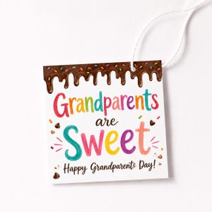 May include: A square white gift tag with a string, featuring a brown chocolate icing drip design at the top with colorful sprinkles. The text reads "Grandparents are Sweet" in multi-colored letters and "Happy Grandparents Day!" in black.