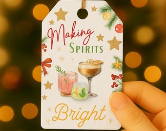 May include: A white gift tag with the text "Making Spirits Bright" in red and yellow script. The tag features illustrations of cocktails, gold stars, and Christmas greenery. A brown string is attached at the top.