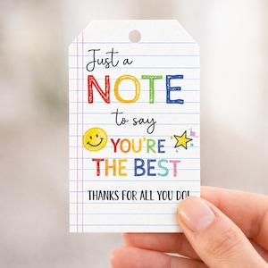 May include: A white gift tag with a hole at the top, featuring colorful text that reads "Just a NOTE to say YOU'RE THE BEST. THANKS FOR ALL YOU DO!" The design includes a smiley face and a star.