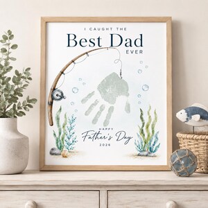 May include: A framed print with the text "I Caught The Best Dad Ever" and "Happy Father's Day 2026." The artwork features a fishing rod, a handprint, bubbles, and aquatic plants in shades of blue and green.