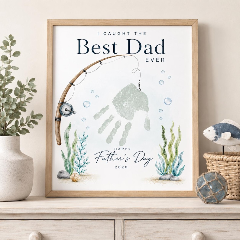 May include: A framed print with the text "I Caught The Best Dad Ever" and "Happy Father's Day 2026." The artwork features a fishing rod, a handprint, bubbles, and aquatic plants in shades of blue and green.