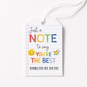 May include: A white rectangular gift tag with a lined notebook paper pattern and a white string. The text reads: Just a NOTE to say YOU'RE THE BEST THANKS FOR ALL YOU DO! It features a yellow smiley face icon and a yellow star icon in colors.