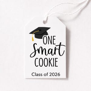 May include: White gift tag with the text "ONE Smart COOKIE" in black script and a graduation cap graphic. The tag also includes "Class of 2026" in a simple font. A yellow tassel hangs from the cap.