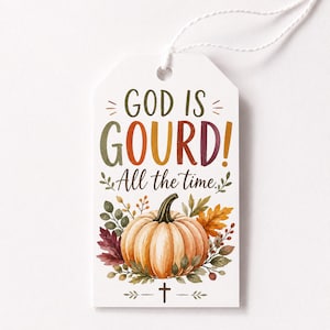 Può includere: Un'etichetta regalo rettangolare bianca con un foro in alto e un cordino bianco. Il testo recita GOD IS GOURD! All the time. Sotto il testo c'è un'illustrazione ad acquerello di una zucca arancione circondata da foglie autunnali e una croce.
