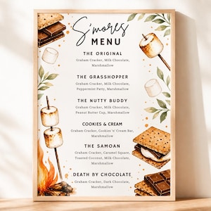 May include: A framed watercolor-style menu titled "S'mores Menu" with illustrations of s'mores ingredients. The menu lists various s'mores recipes, including "The Original," "The Grasshopper," and "The Nutty Buddy." The frame is a light brown color.