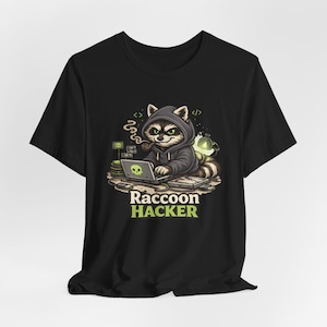 Könnte beinhalten: Schwarzes T-Shirt mit einem Cartoon-Waschbären, der einen Kapuzenpullover trägt und eine Pfeife raucht, während er an einem Laptop arbeitet. Das Design enthält den Text "Raccoon Hacker" in Grün und Gelb sowie Computer-Grafiken.