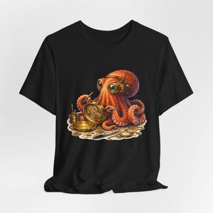 Op de afbeelding: Zwart T-shirt met een gedetailleerde illustratie van een oranje octopus met een bril en een uurwerk. De octopus is omringd door gereedschap en een gouden schaal, wat een steampunk esthetiek creëert.