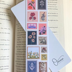 May include: A floral bookmark with postage stamp designs showcasing flower illustrations in pink, orange, blue, and yellow. The bookmark is rectangular and has the text "Floral" and "Front & Back".