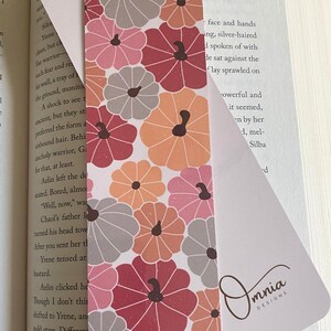 Puede incluir: Marcap&aacute;ginas decorativo con un dise&ntilde;o de calabazas en tonos rosa, naranja y gris. El marcap&aacute;ginas est&aacute; insertado en un libro. Los textos "Pumpkin Patch" y "Front & Back" son visibles.