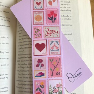 May include: A pink bookmark with a stamp design featuring hearts, flowers, and the words "Love" and "Sunshine." The bookmark is in a book, with the text "Pink Overload" and "Front & Back" visible.