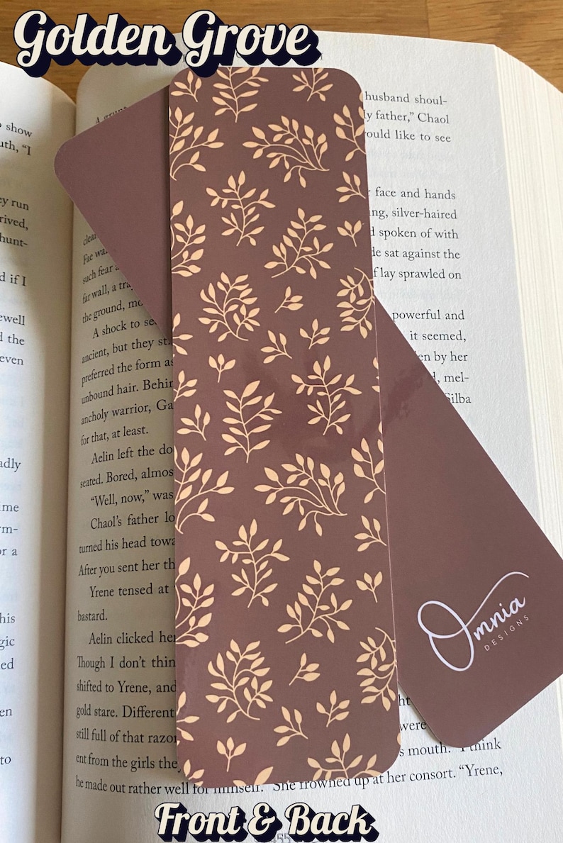Puede incluir: Un marcap&aacute;ginas marr&oacute;n con un dise&ntilde;o floral beige. El marcap&aacute;ginas es rectangular con esquinas redondeadas y el texto "Front & Back". El logotipo "Omnia Designs" es visible.