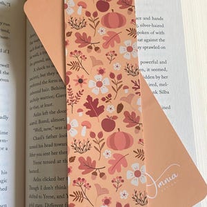 Puede incluir: Marcap&aacute;ginas con tem&aacute;tica oto&ntilde;al con fondo melocot&oacute;n y un patr&oacute;n de calabazas, hojas y flores. El marcap&aacute;ginas se muestra en un libro abierto. Los textos "Fall Foliage" y "Front & Back" son visibles.