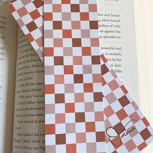 Puede incluir: Dos marcap&aacute;ginas rectangulares con un dise&ntilde;o de tablero de ajedrez en tonos marr&oacute;n, naranja y blanco. El texto "Autumn Checkers" est&aacute; en la parte superior. El marcap&aacute;ginas inferior tiene el texto "Front & Back" y un logotipo.