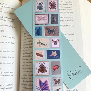 May include: A light blue bookmark with insect illustrations designed as postage stamps. The bookmark has the word "Entomology" at the top and "Front & Back" at the bottom. The bookmark is placed in an open book.