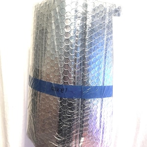 May include: A rectangular package wrapped in clear bubble wrap and secured with blue tape. The text "pixel" is written on the tape. The package is held by a hand.