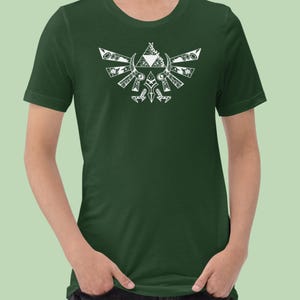 May include: A dark green t-shirt featuring a white graphic design. The design is a stylized crest with geometric and floral elements. The shirt has short sleeves and a crew neck.