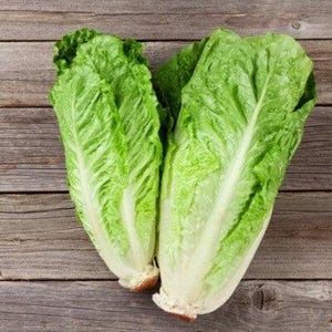 Könnte beinhalten: Zwei frische Köpfe Römersalat mit leuchtend grünen Blättern und weißen Stielen. Der Salat wird auf einer rustikalen Holzoberfläche präsentiert, die die natürlichen Texturen und Farben des Produkts hervorhebt.