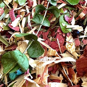 Puede incluir: Primer plano de una mezcla de botánicos secos. La imagen presenta hojas de eucalipto verdes, virutas de madera rojas y beige y hierbas secas. También se ve una pequeña baya oscura. La disposición tiene una estética natural y terrosa.