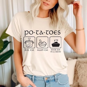 Puede incluir: Camiseta color crema con el texto "po-ta-toes" sobre tres ilustraciones en blanco y negro. Las ilustraciones muestran patatas hirviendo, hechas puré y en un guiso. El texto debajo dice "BOIL 'EM", "MASH 'EM" y "STICK 'EM IN A STEW".