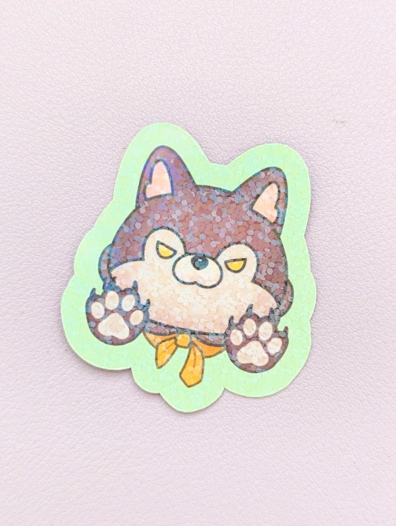 May include: A glittery sticker featuring a dark brown and cream-colored cartoon dog with yellow eyes and a yellow bow tie. The dog is depicted with its paws raised against a light green background, creating a playful and expressive character design.