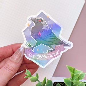 May include: A sticker featuring a stylized crow with a futuristic design, set against a diamond-shaped background with a galaxy theme. The crow has a red visor and the text "Hot Crow Walk" on a banner.