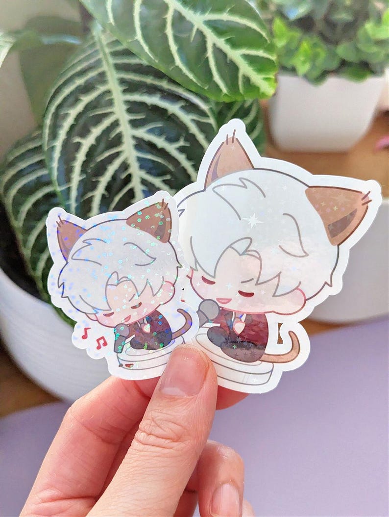 May include: Two holographic stickers featuring anime-style cat characters. The characters have white hair, brown ears, and are wearing suits. One is singing into a microphone, and musical notes are visible. The stickers are held in front of a plant.
