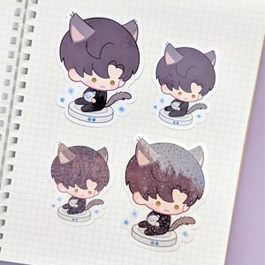 May include: Four stickers featuring a cartoon character with cat ears and dark hair. The character is holding a small, round object and sitting on a circular platform. Each sticker has a different pattern on the hair. Blue snowflakes surround the platform.