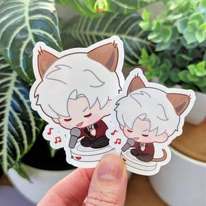May include: Two stickers featuring a cartoon character with white hair and cat ears, wearing a maroon suit and singing into a microphone. The stickers are held in front of a background of green plants.