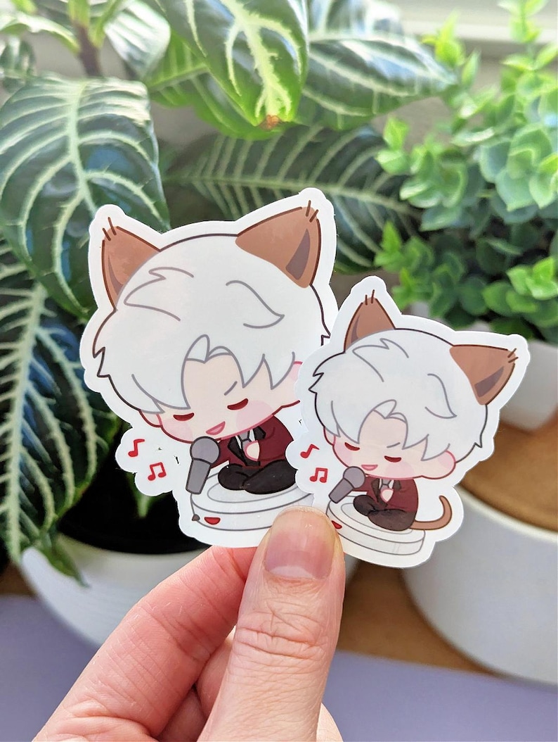 May include: Two stickers featuring a cartoon character with white hair and cat ears, wearing a maroon suit and singing into a microphone. The stickers are held in front of a background of green plants.