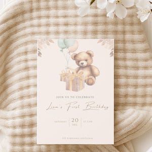 Op de afbeelding: Een rechthoekige verjaardagsuitnodigingskaart met een aquarelillustratie van een bruine teddybeer die een cadeau en ballonnen vasthoudt. De tekst luidt: JOIN US TO CELEBRATE Liam's First Birthday SATURDAY 20 DEC AT 2 PM 123 Bidstown, california.