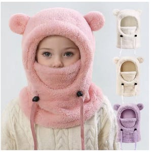 Peut inclure: Un chapeau rose en forme de cagoule avec des oreilles d'ours et un couvre-visage. Le chapeau a des cordons de serrage réglables et est porté par un enfant. D'autres chapeaux blancs, crème et lavande sont affichés à droite.