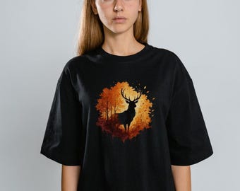 May include: Black t-shirt featuring a silhouette of a deer with large antlers set against a backdrop of autumn foliage in shades of orange, red, and yellow. The graphic is centered on the front of the shirt.