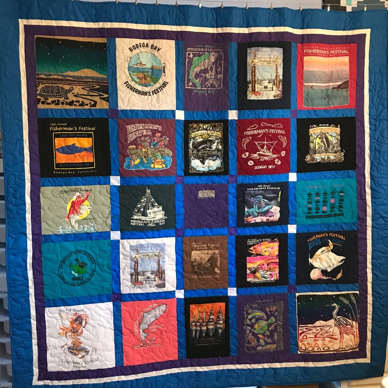 May include: A quilt made from a collection of t-shirts featuring the Bodega Bay Fisherman's Festival. The quilt is made up of 25 squares, each with a different design. The designs include fish, boats, and other nautical imagery. The quilt is a great way to commemorate the festival and show your support for the community.