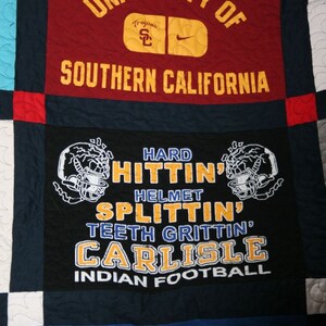 May include: A quilt made of different fabric squares. The squares feature logos and text from the University of Southern California, including the words "Trojans", "Hard Hitting", "Helmet Splitting", "Teeth Gritting", "Carlisle", and "Indian Football".