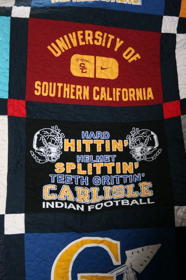 May include: A quilt made of different fabric squares. The squares feature logos and text from the University of Southern California, including the words "Trojans", "Hard Hitting", "Helmet Splitting", "Teeth Gritting", "Carlisle", and "Indian Football".