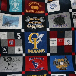 May include: A quilt made from a variety of t-shirts, featuring different logos and designs. The quilt is made up of squares, each with a different design. Some of the designs include the words "One Team One Dream", "Put On Your Game Face", and "The Tribe Is Alive!"