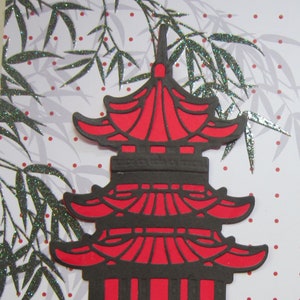 May include: A red and black paper craft of a traditional Chinese pagoda with a white background with black and silver glitter bamboo leaves and red dots.