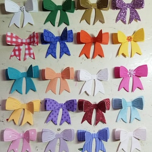 May include: Assortment of 18 paper bows in various colors and patterns, including red and white gingham, teal, purple glitter, and pink with a flower accent. The bows are cut from cardstock and are perfect for crafting and scrapbooking.
