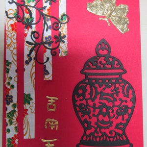 May include: A red card with a black and white floral design, a gold butterfly, and a black and white vase with a gold inscription. The inscription reads "Happy New Year".