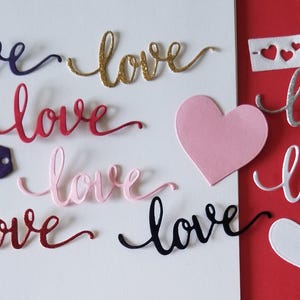 May include: Assortment of paper cutouts in various colors, including black, white, red, pink, gold, and silver. The cutouts are in the shape of the word "love" and hearts.