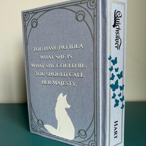 May include: A hardback book titled "Quicksilver" with a pale blue cover. The cover features a white fox silhouette and text that reads "YOU HAVE NO IDEA WHAT SHE IS. WHAT SHE COULD BE. YOU SHOULD CALL HER MAJESTY." The spine has teal butterflies.