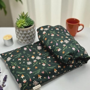 Puede incluir: Dos almohadillas t&eacute;rmicas con estampado floral verde oscuro. Las almohadillas tienen un patr&oacute;n de flores blancas, rosas y naranjas con hojas verdes. Una peque&ntilde;a planta suculenta en una maceta gris, una vela y una taza est&aacute;n en el fondo.