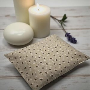K&ouml;nnte beinhalten: Ein beiges Kissen mit Martini-Gl&auml;ser-Muster, brennenden Kerzen und einer wei&szlig;en Seife auf einer Holzoberfl&auml;che. Das Kissen hat ein sich wiederholendes Muster aus wei&szlig;en Martini-Gl&auml;sern mit braunen Details. Zwei brennende Kerzen und eine wei&szlig;e Seife sind im Hintergrund.